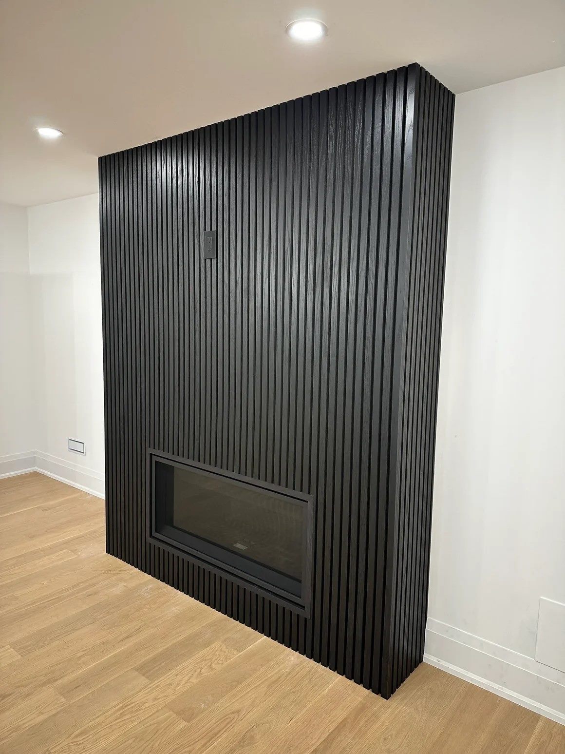 Full-height black slat surround wrapping a bump-out wall with a linear gas fireplace set into it.