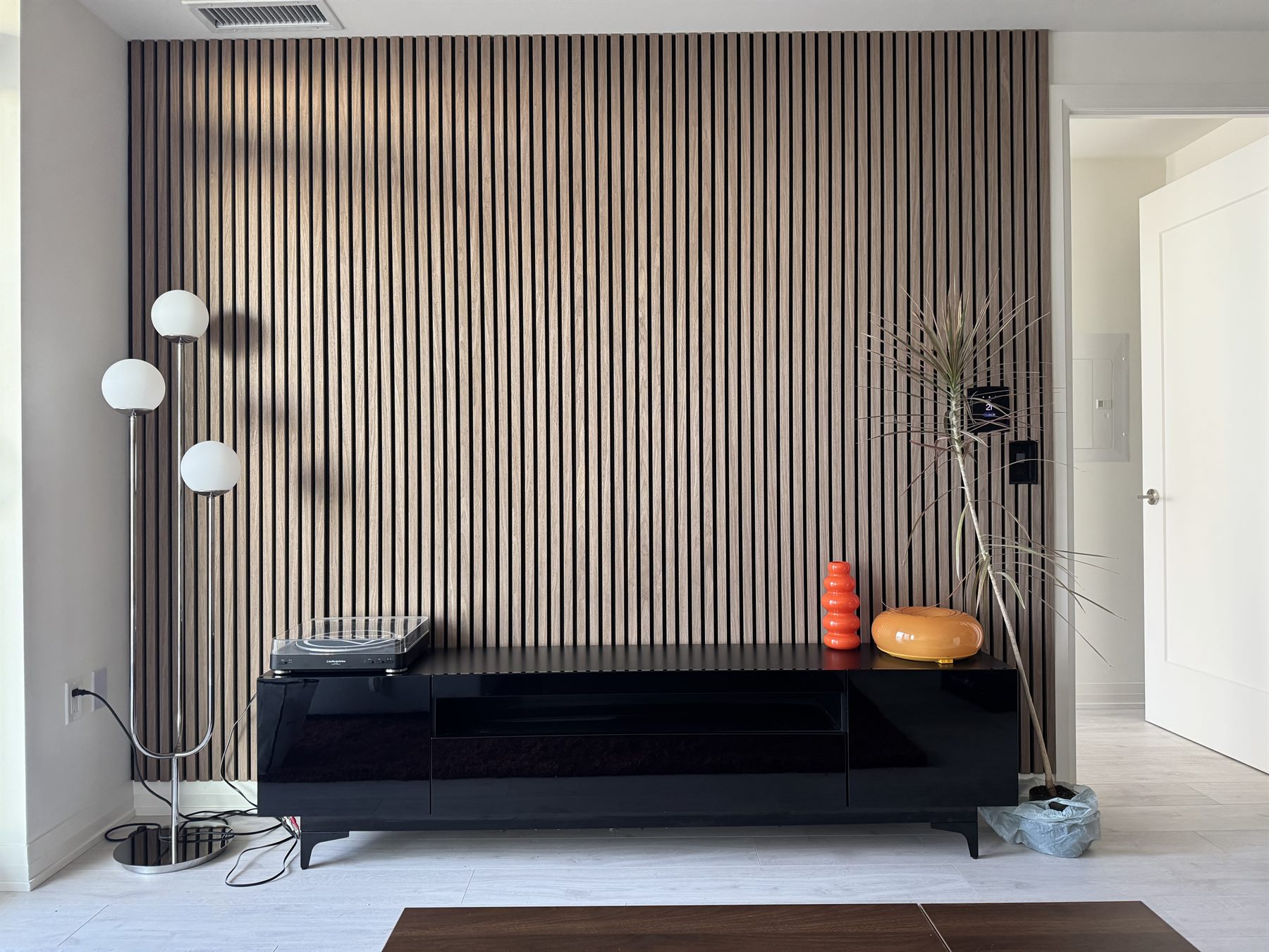 Living room with a full-height oak slat wall behind a long black console, dimmed.