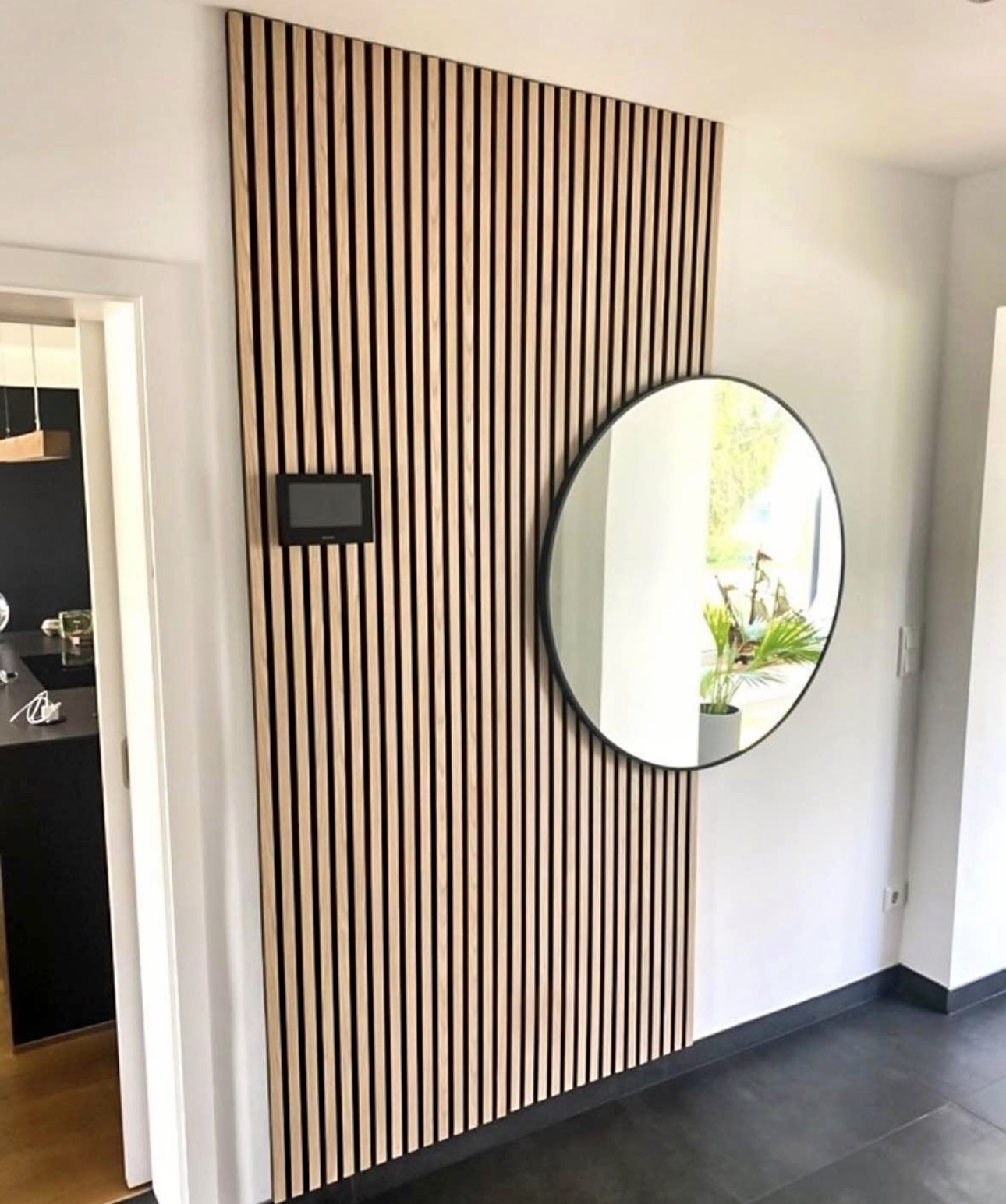 Light oak slat entryway panel with a round black mirror mounted at its centre.