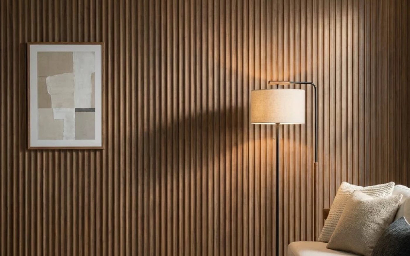 A living room wall clad floor to ceiling in warm walnut-toned wood composite slats, with a framed print and a floor lamp against it.