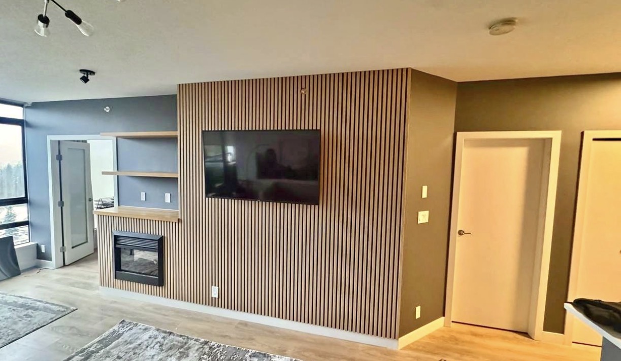 Oak slats wrapping a bump-out wall around a recessed fireplace, television, and floating shelves.