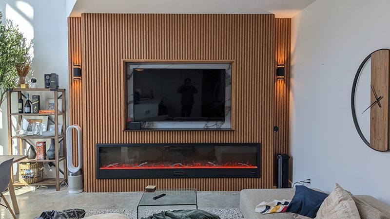 Fluted oak feature wall with a mounted television, marble surround and a long linear electric fireplace beneath.