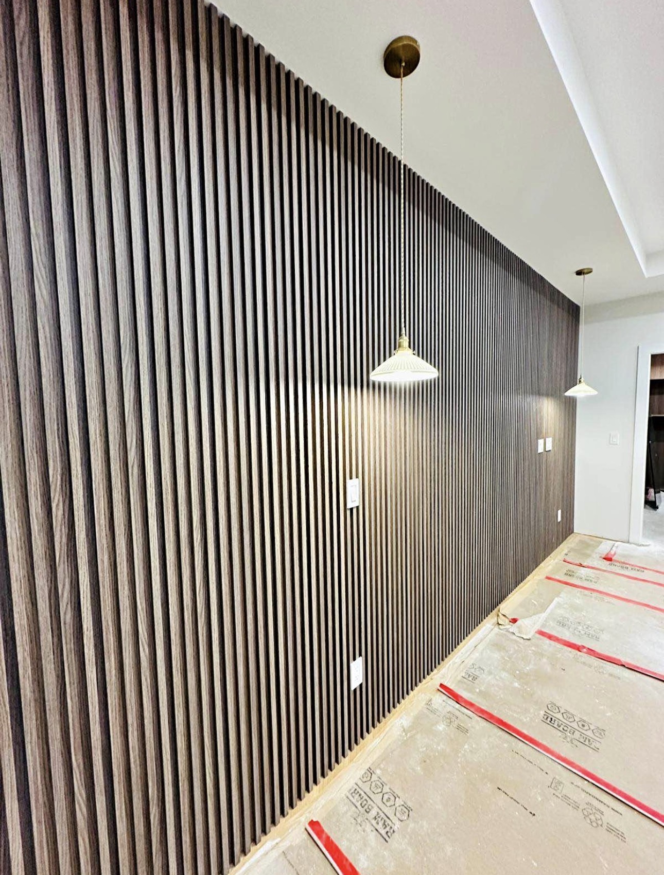 Dark walnut full-height slat wall along a hallway, floor protection paper still down as the install nears completion.