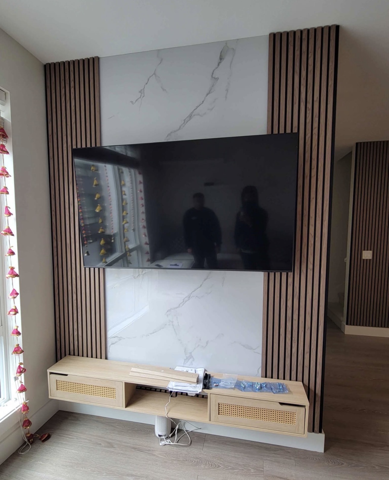 TV wall with a marble centre panel flanked by oak slat columns and a floating rattan console.