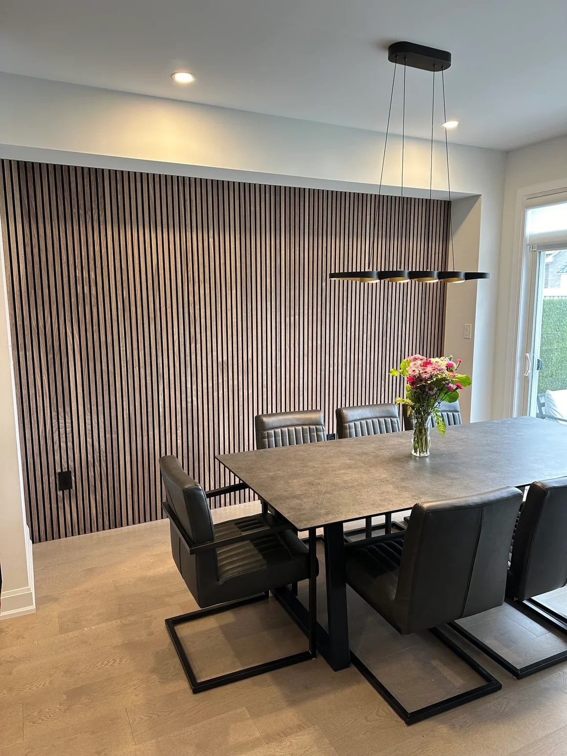 Dining room feature wall in dark walnut slats running the full height behind a stone-topped table.