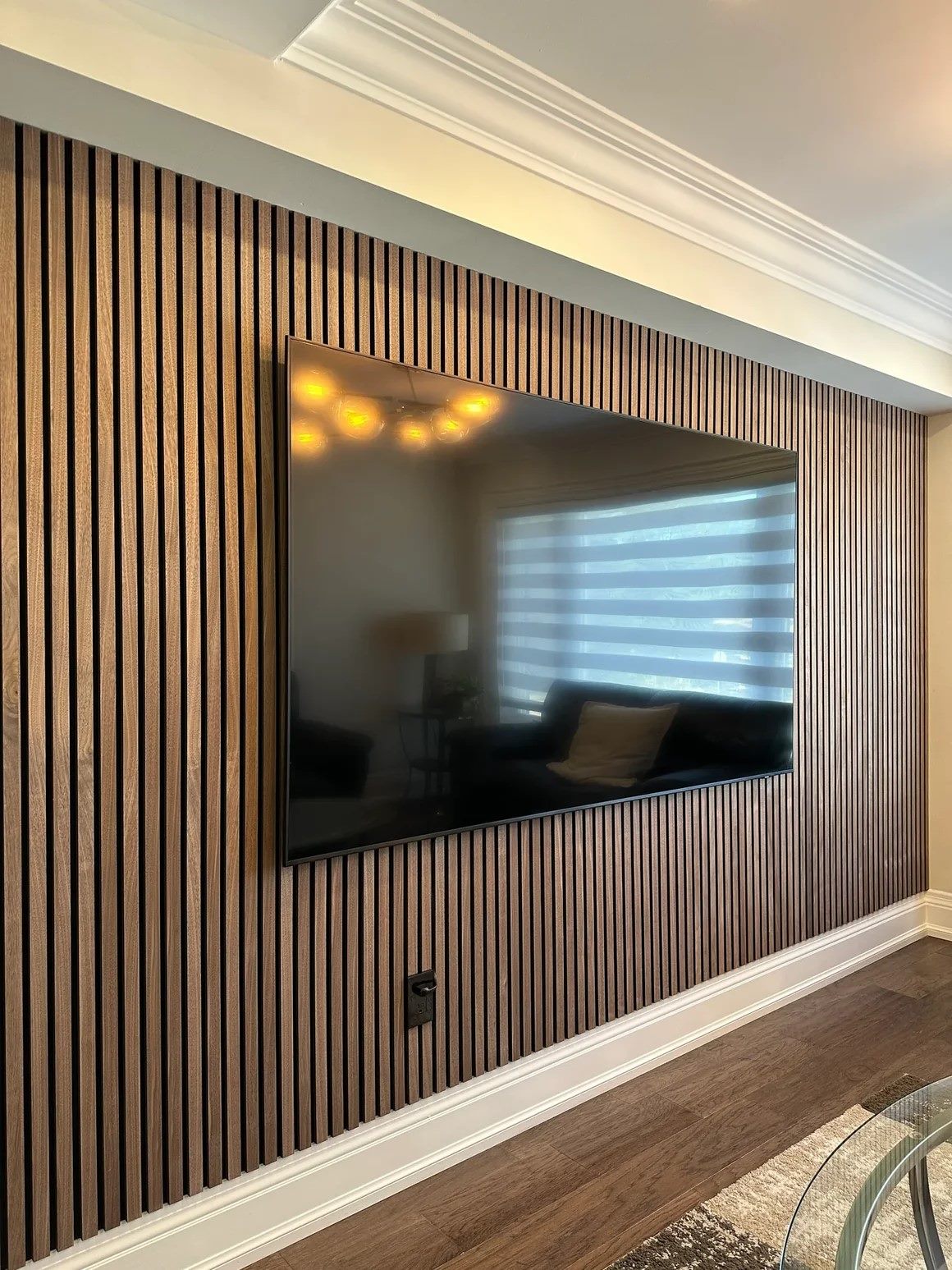 Family room feature wall in natural walnut veneer slats with a large television recessed flush into the panelling.