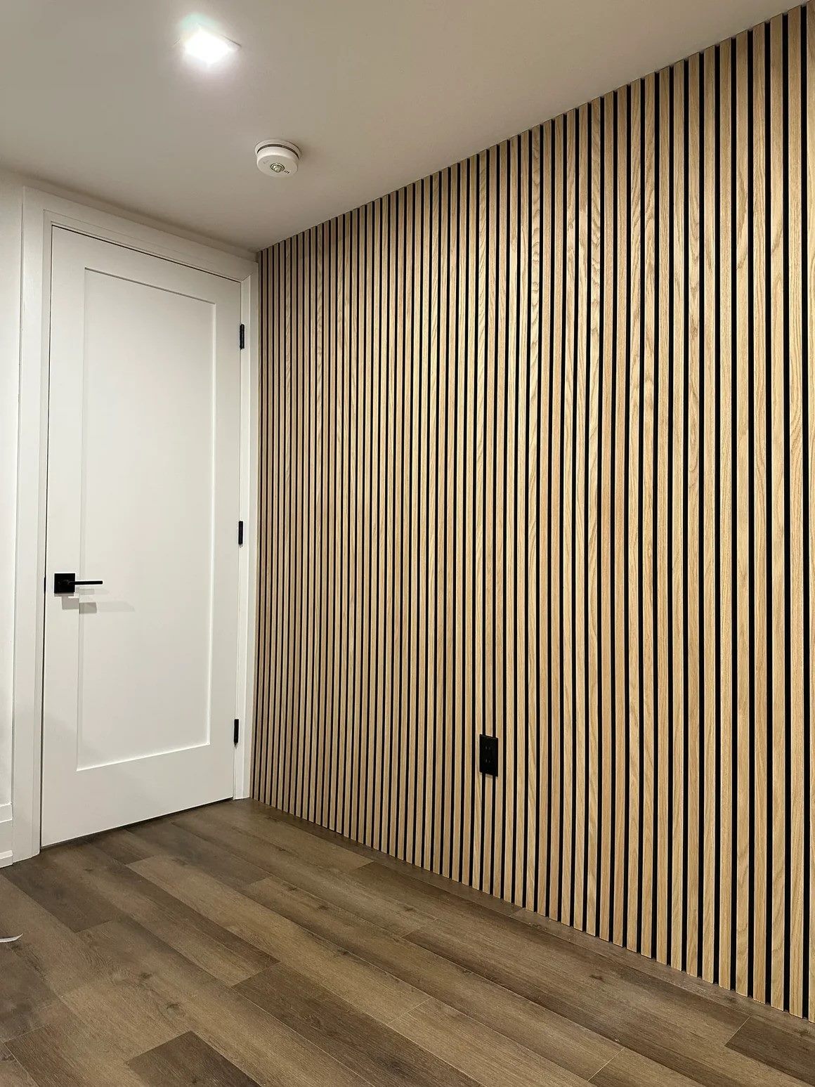 Hallway with full-height natural white oak slat panelling running beside a white door.